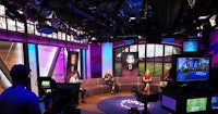 a television studio with people sitting on couches in front of a purple screen