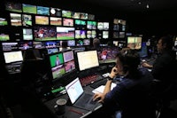 a group of people sitting in a room with many monitors